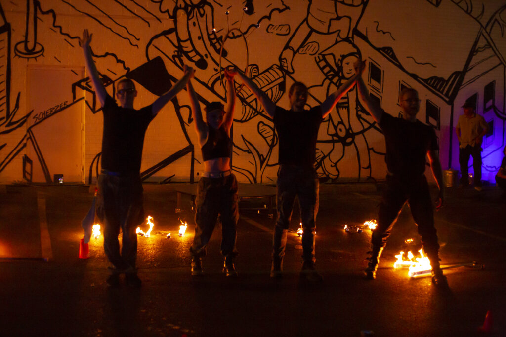 People celebrating with arms raised in a dark, fiery environment.