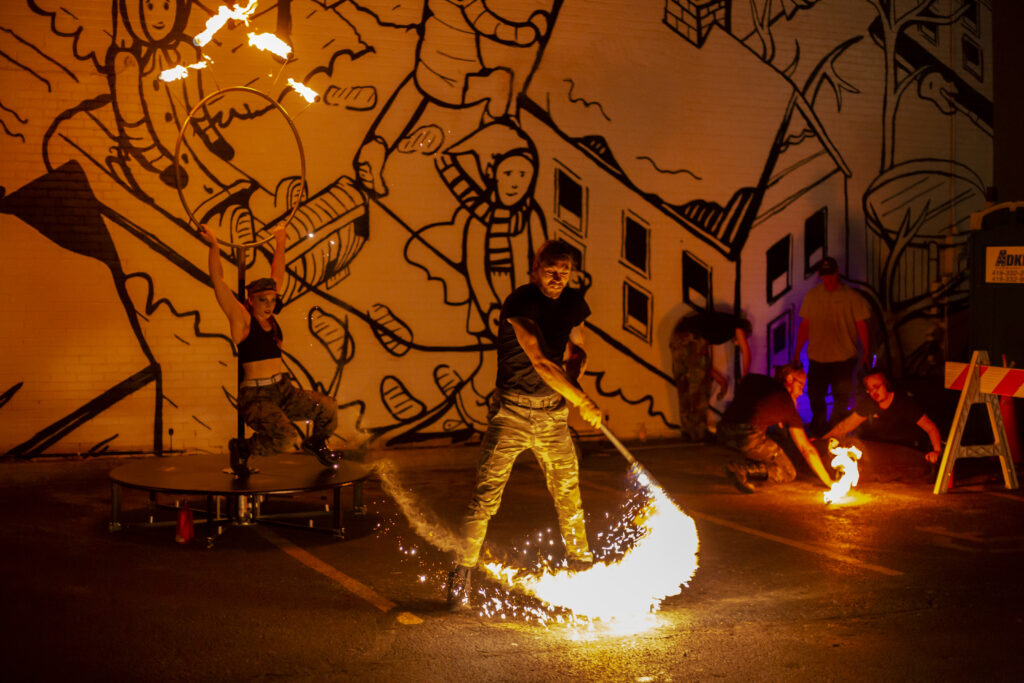 A person performing fire spinning at night near buildings.