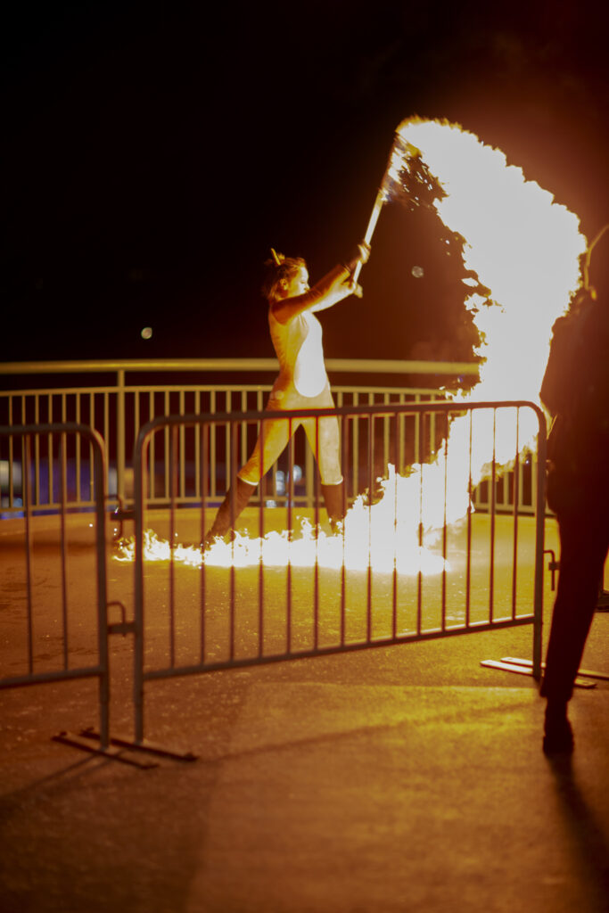 A performer breathing fire behind a safety barrier at night.