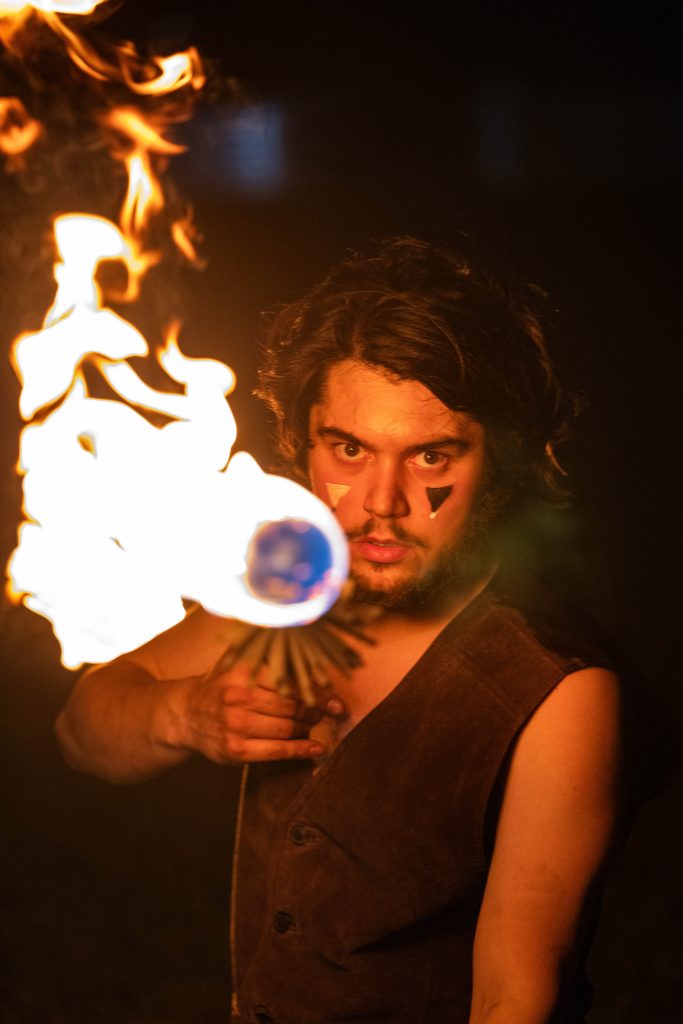 A man aiming a flaming gun with intense expression.