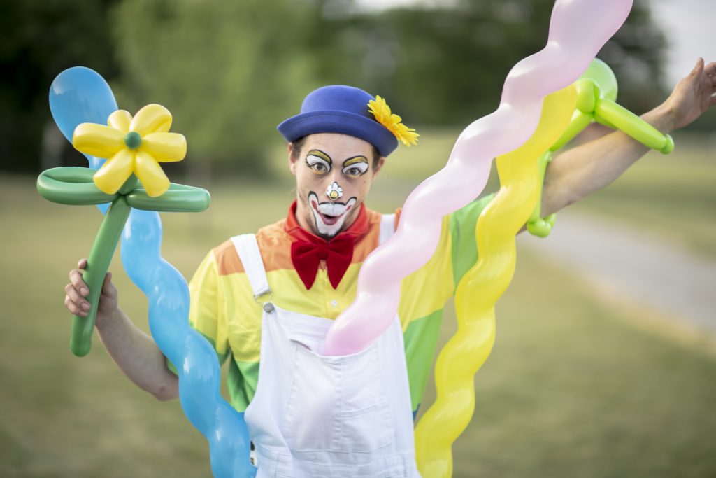 A clown holding colorful twisted balloons outdoors.