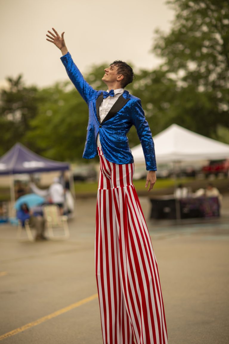 Performer on stilts in patriotic outfit at outdoor event.
