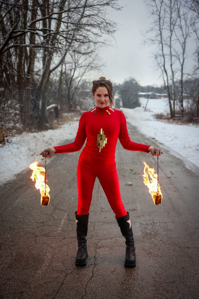 Person in red suit holding fire torches on a snowy road.