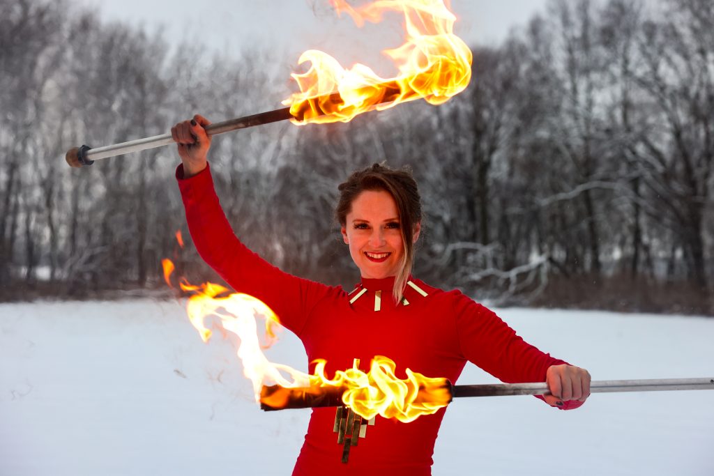 A woman performing fire twirling outdoors in winter.