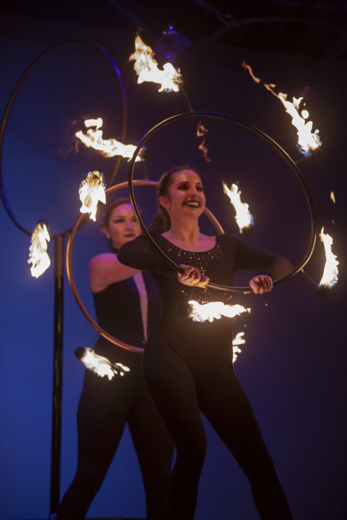 Two women performing a fire hoop dance at night.
