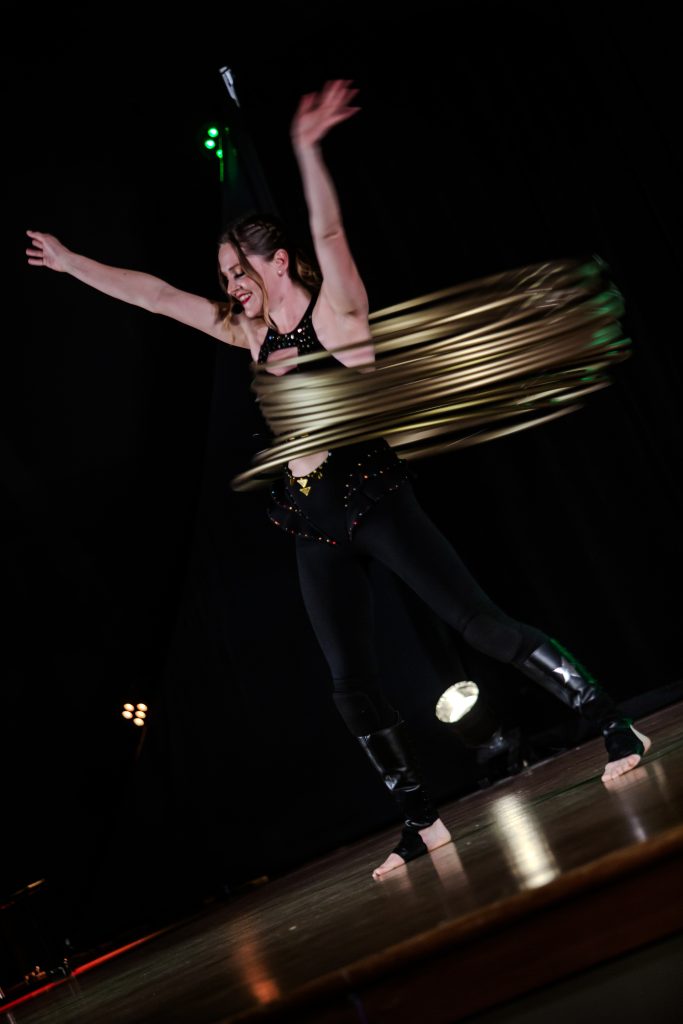 A person spinning multiple hula hoops on their waist under stage lights.
