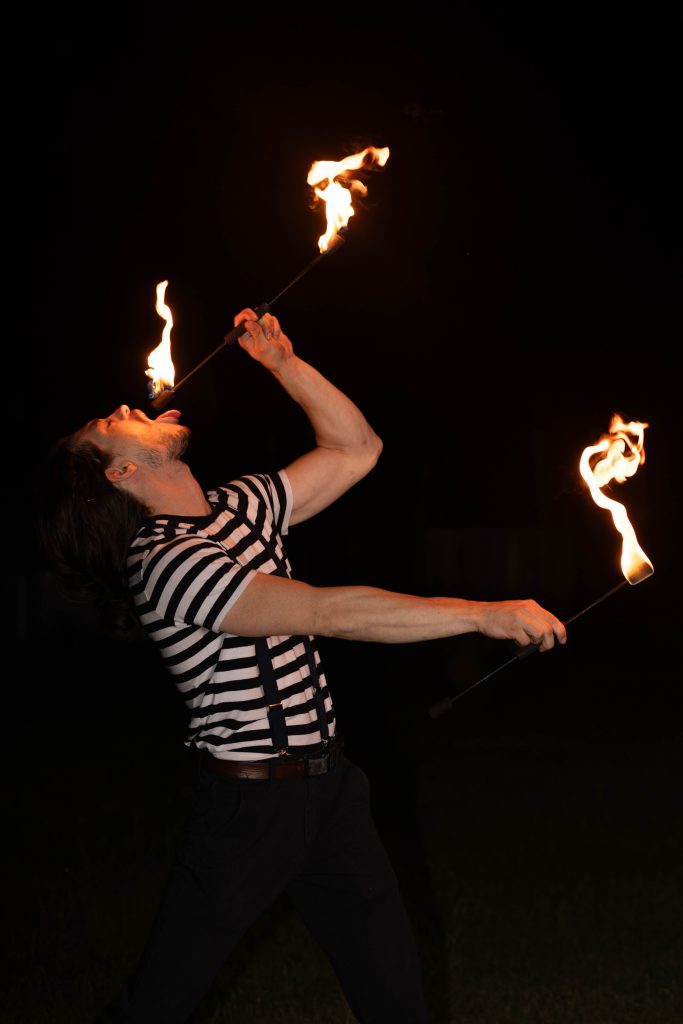 A man performs fire breathing at night wearing a striped shirt.