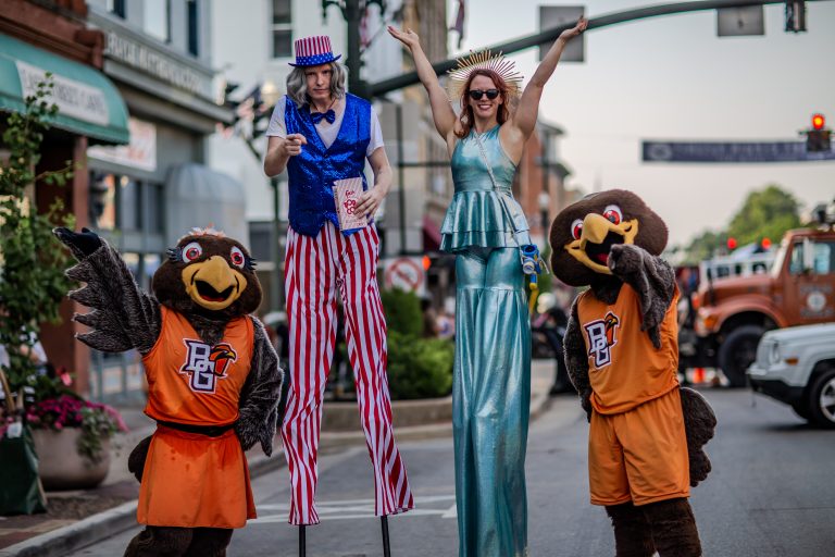 Two performers on stilts with two people in mascot costumes on a city street.