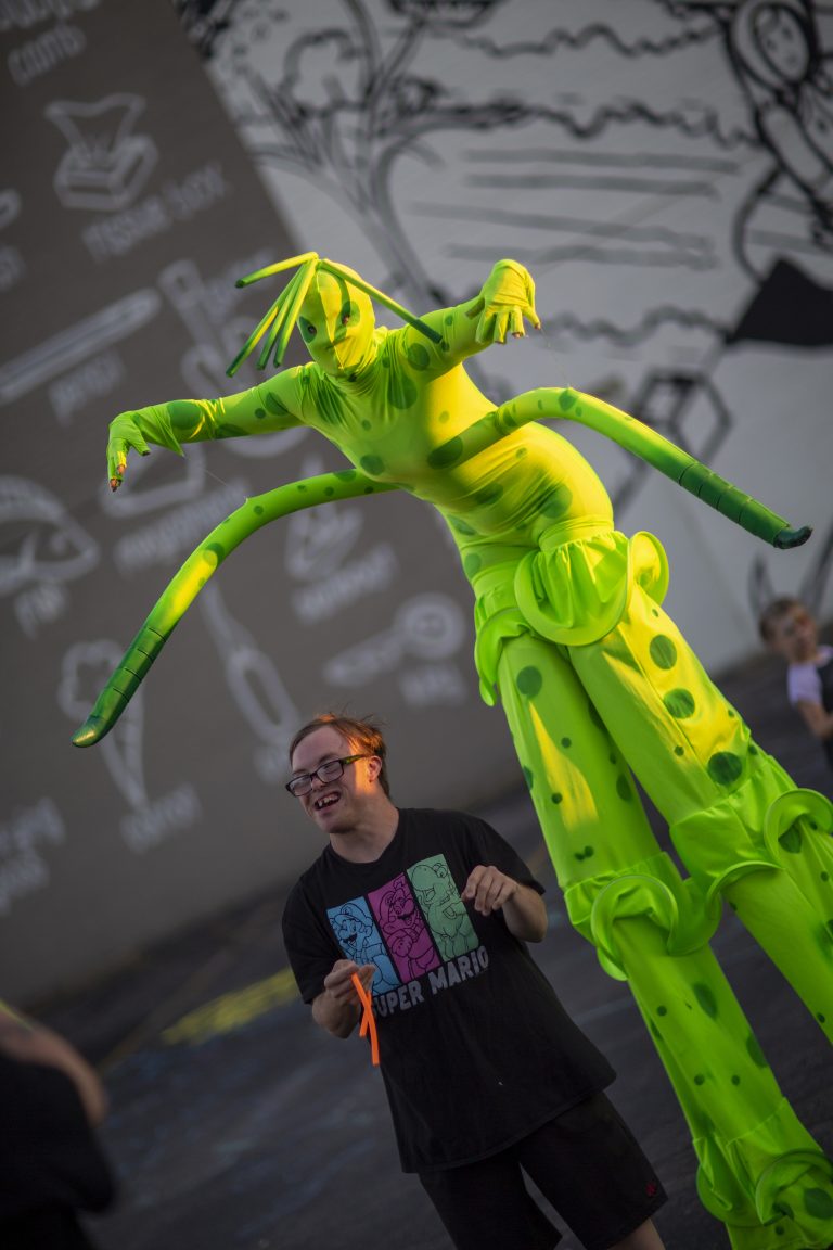 A performer on stilts in a green costume with yellow accents.