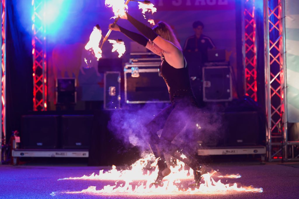 A performer dances barefoot on fire on stage.