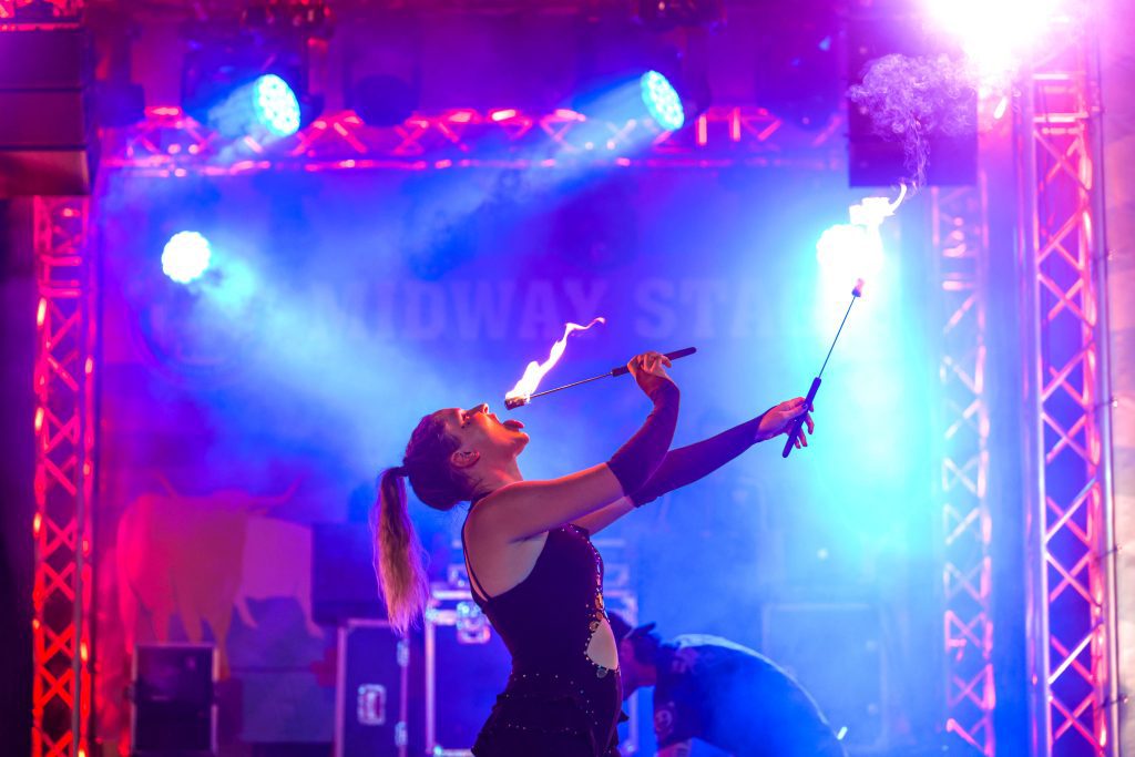 A performer breathing fire on stage with colorful lights.