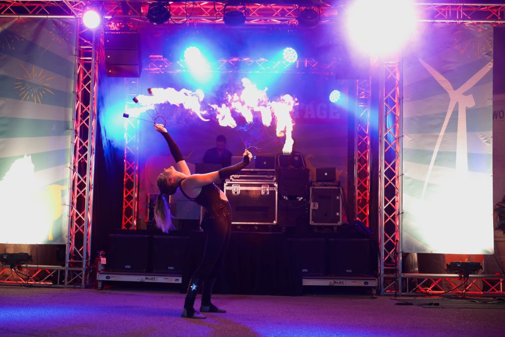 A fire performer breathing flames on stage with colorful lights.