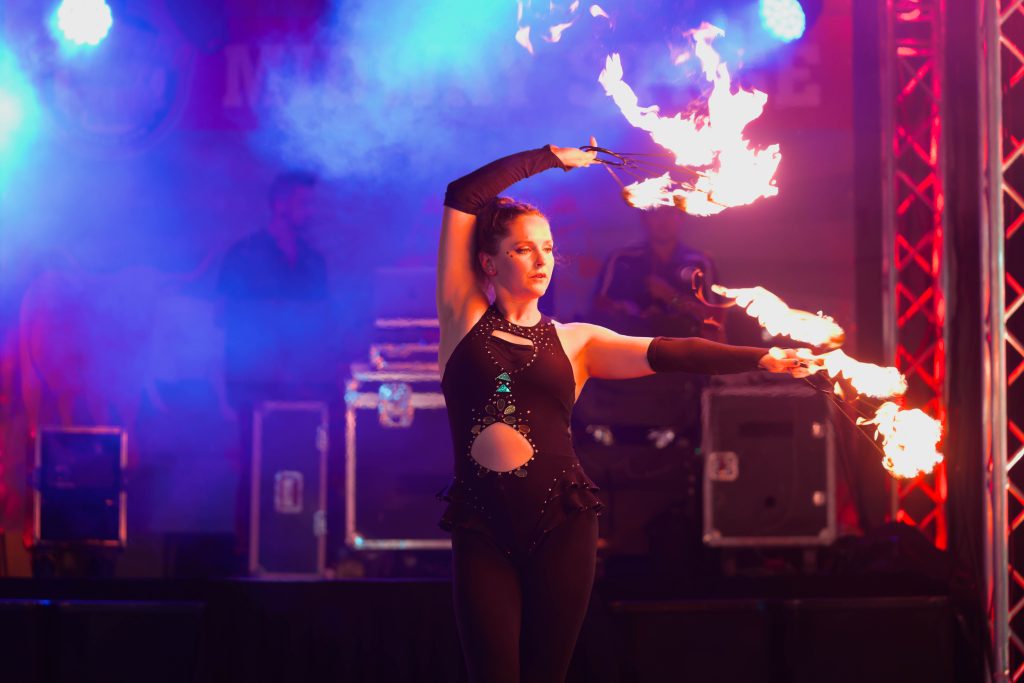 A performer manipulating fire on stage with colorful lighting.