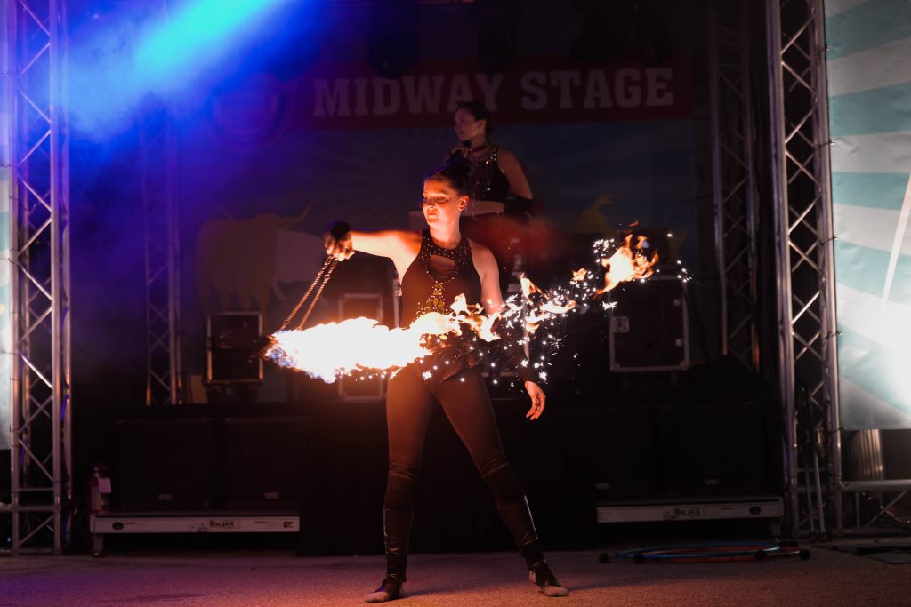 A performer spins fire poi on stage with sparks flying.