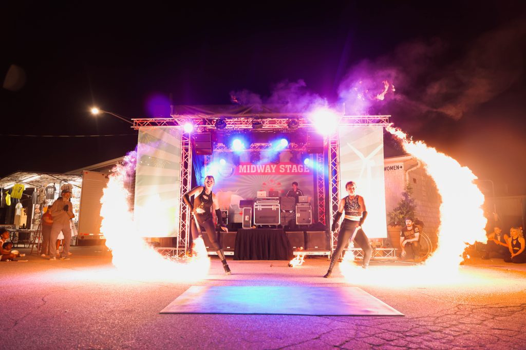 A nighttime outdoor concert with fire effects and musicians on stage.