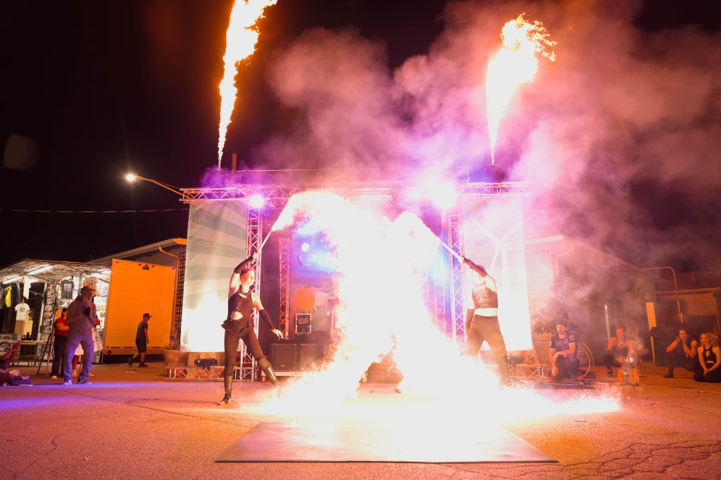 Two performers with fire and smoke at night on a street.