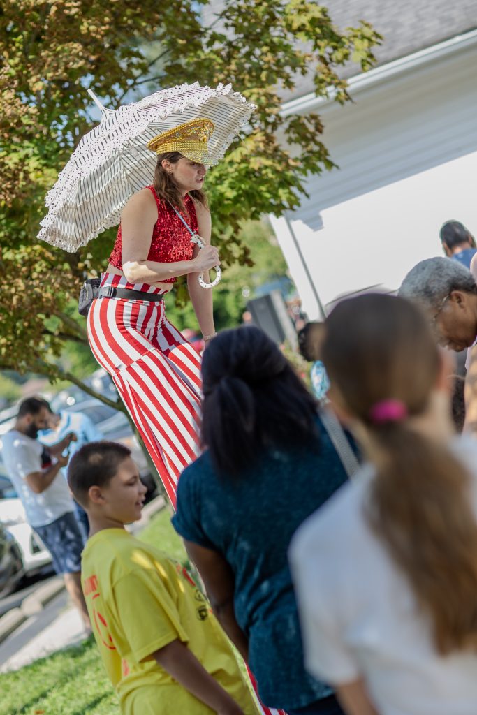 A street performer on stilts entertains a crowd with a parasol.