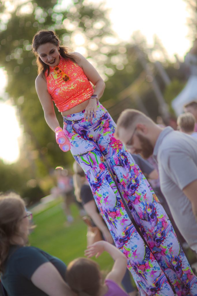 A woman on stilts wearing colorful pants and an orange top.