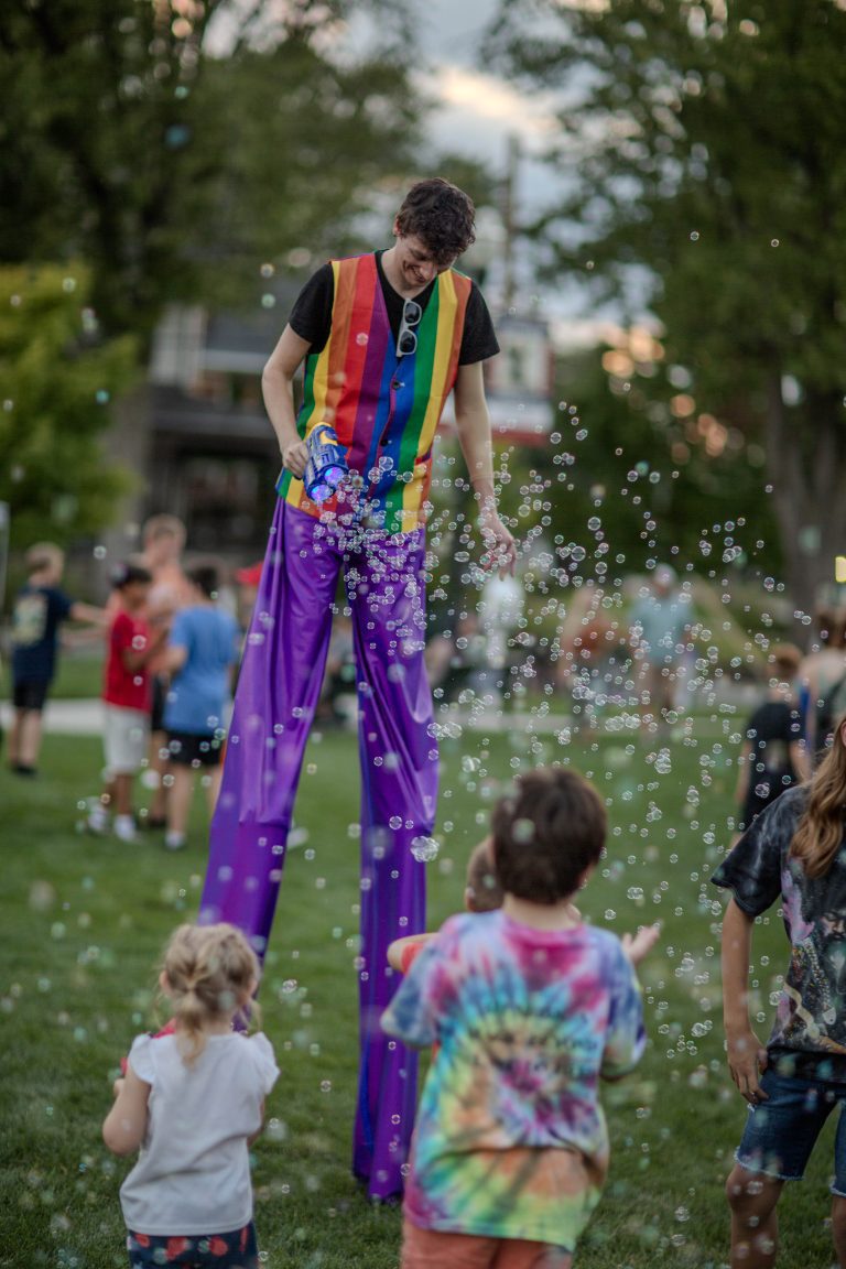 A person on stilts wearing colorful clothes entertains children outdoors.
