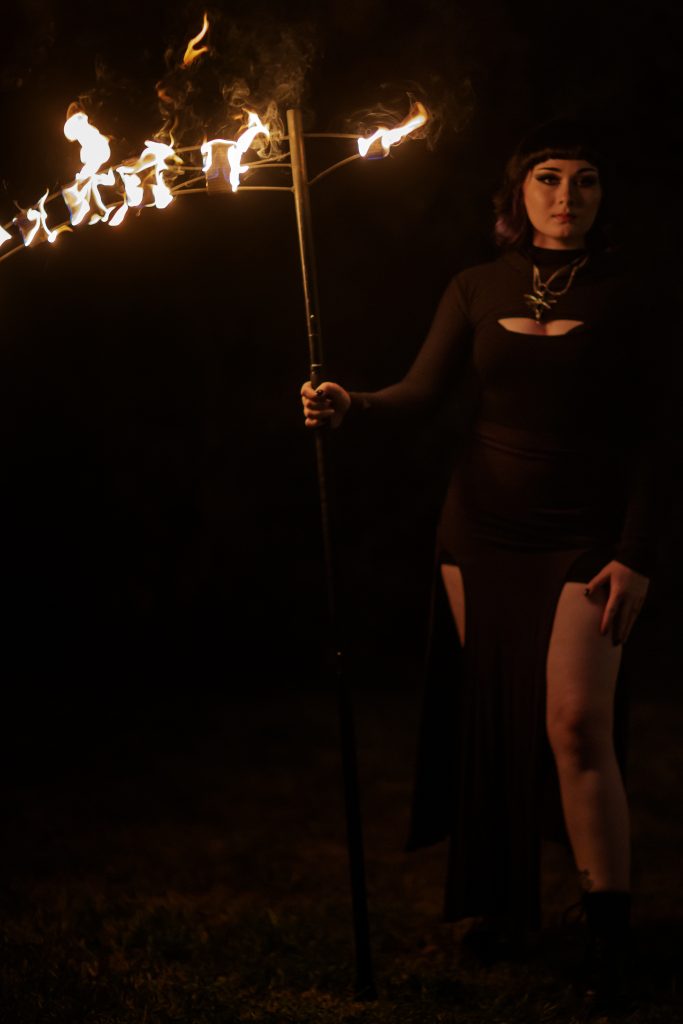 A person in a black dress holding a lit torch in the dark.