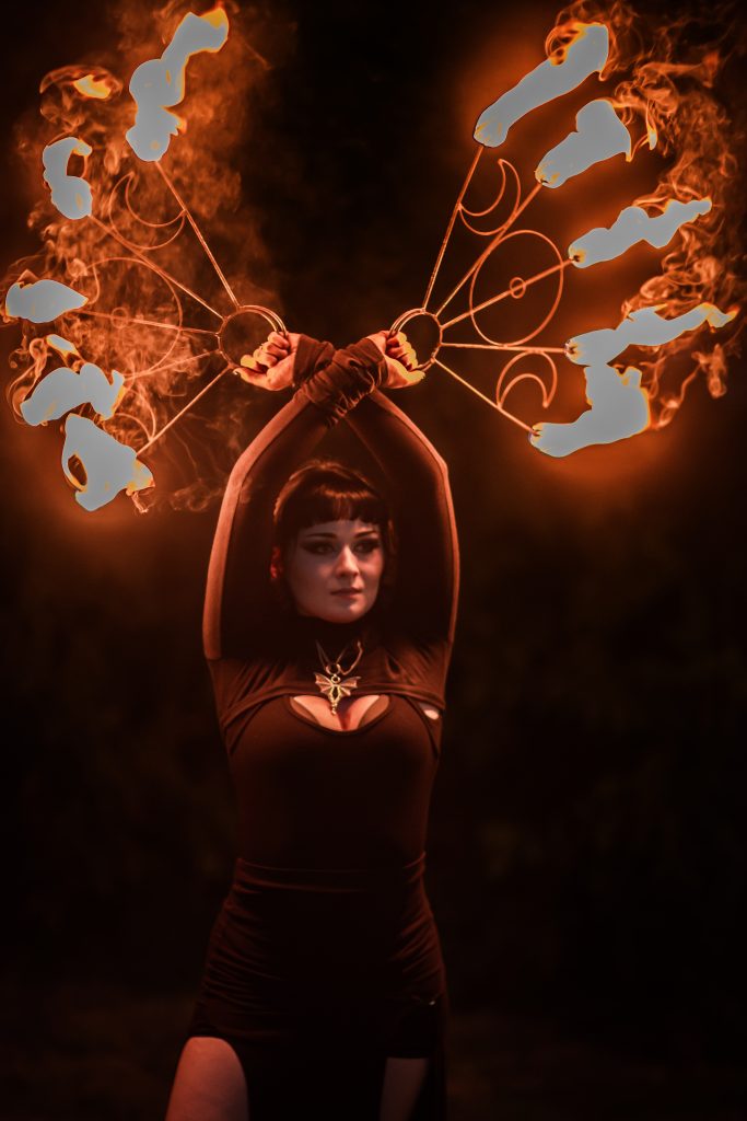 A woman performs with flaming hoops in a dark setting.
