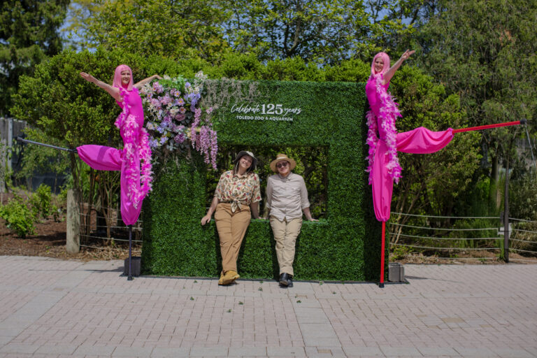 Two children standing between two performers on stilts dressed in pink.