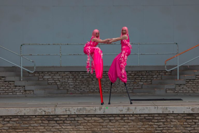 Two performers on stilts dressed in bright pink costumes.