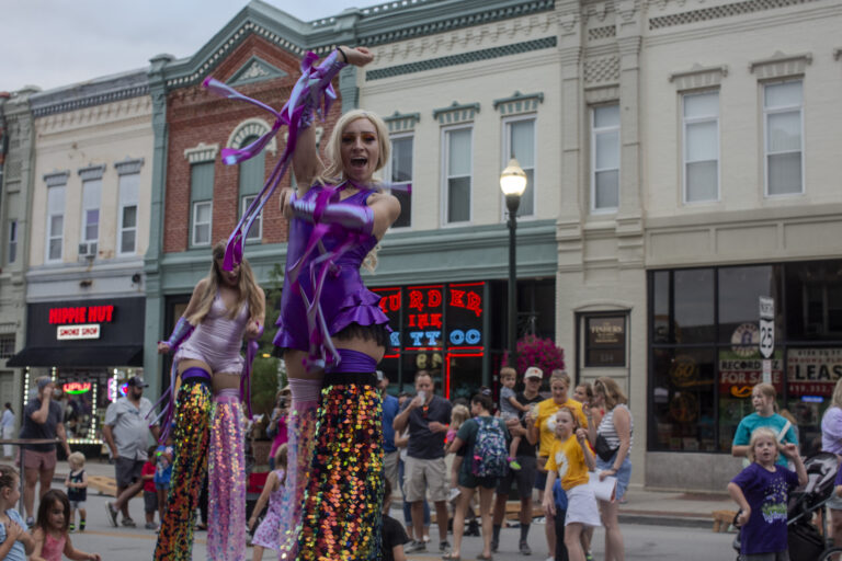 Performers on stilts in colorful costumes dancing.