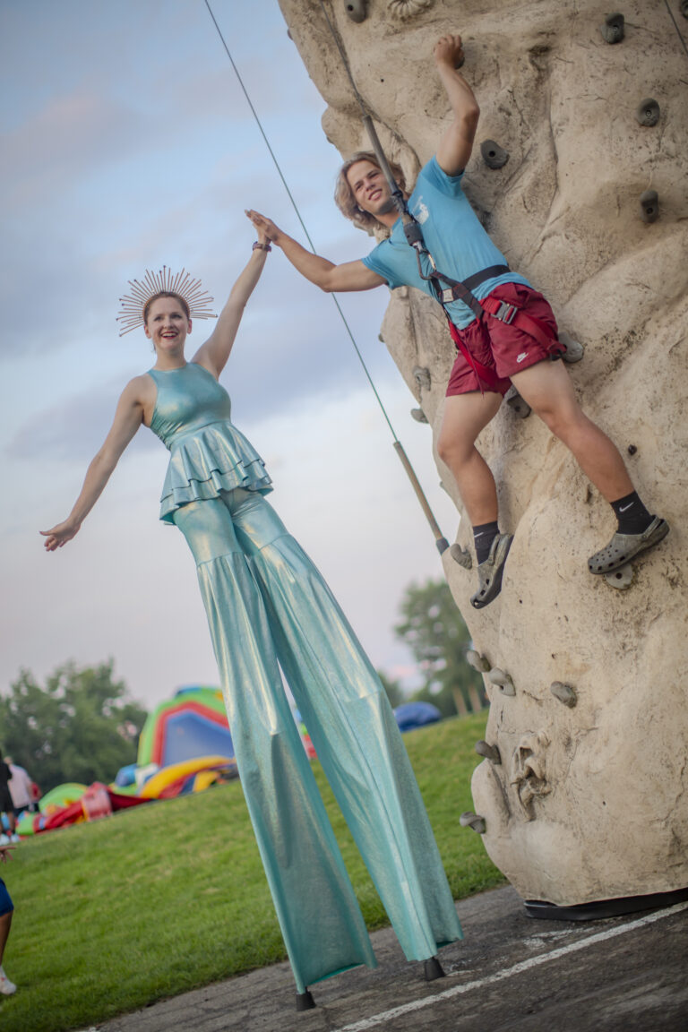 Performer on stilts and climber on wall.