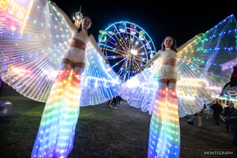 Stilt walkers with illuminated wings at festival.