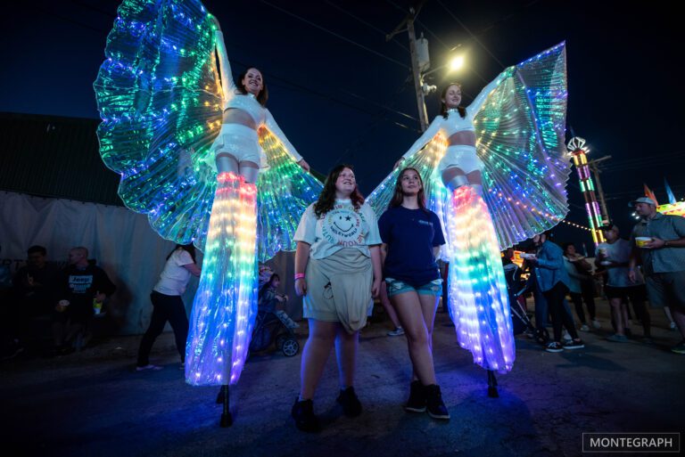Girls posing with LED-winged stilt performers