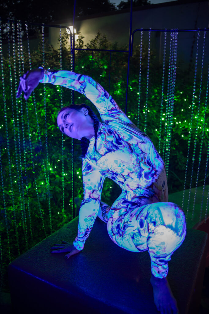 Person in glowing patterned suit stretching on platform