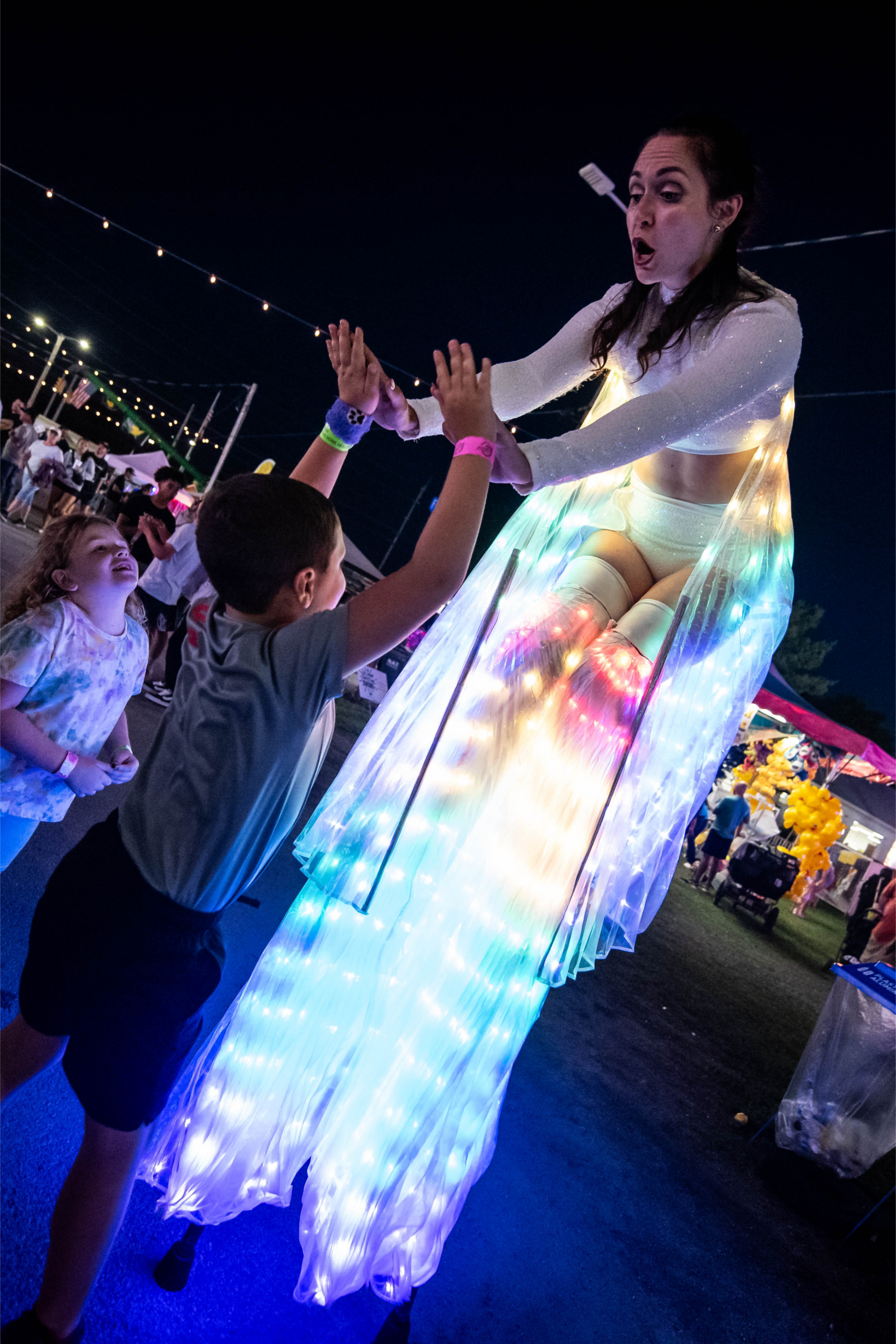 Glowing LED stilt performer entertaining children