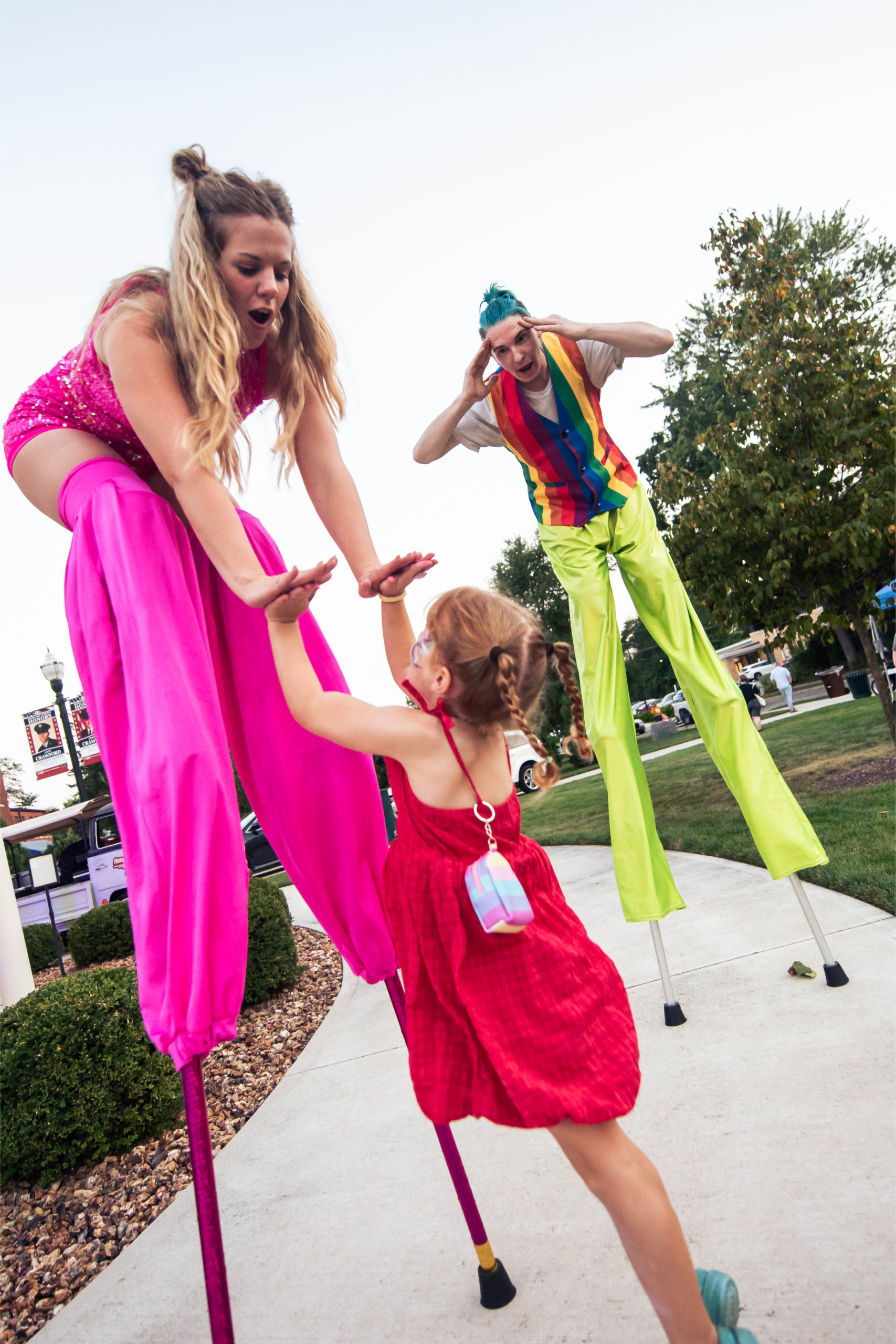 Child reaching up to colorful stilt walkers