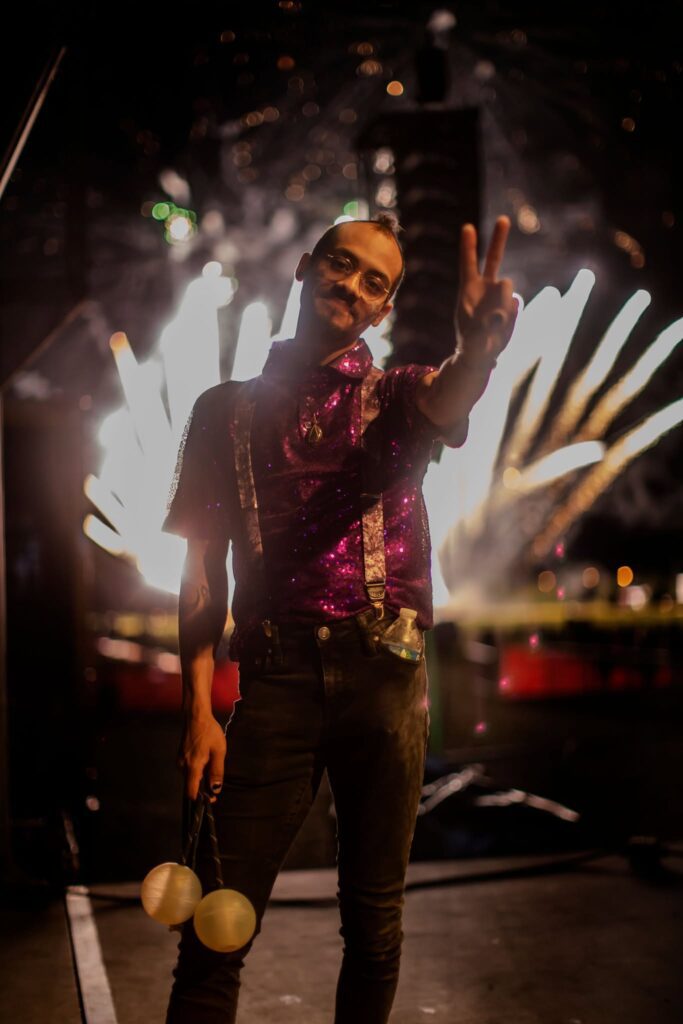 Sequined performer holding juggling balls, fireworks