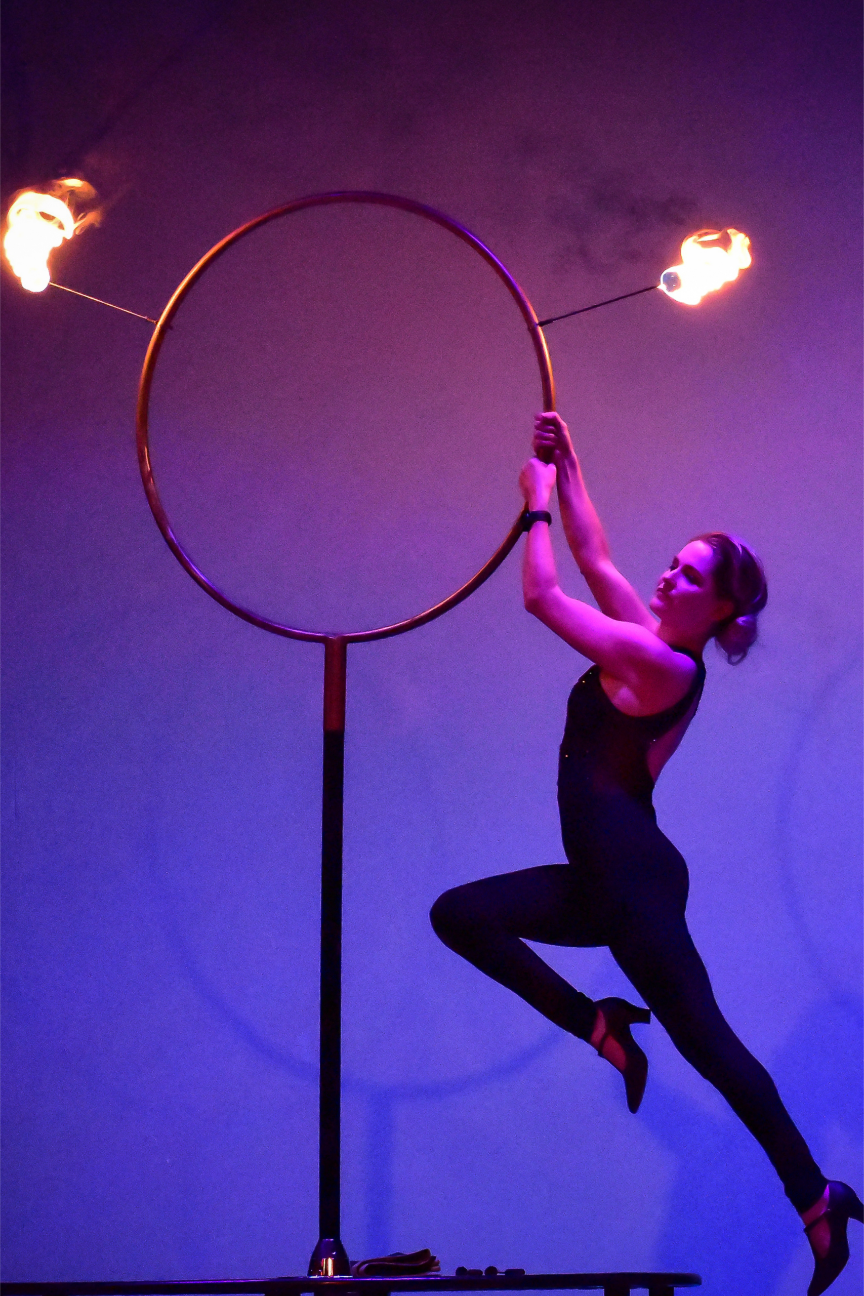 Purple-lit aerialist suspended from flaming hoop