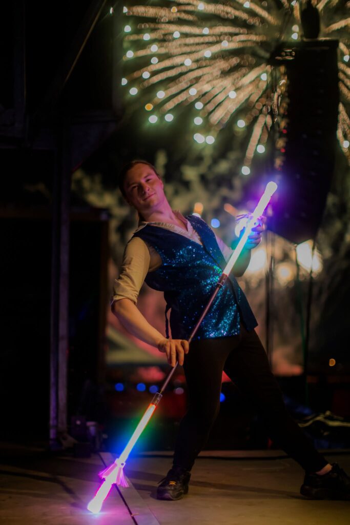 Performer twirling rainbow LED staff, fireworks