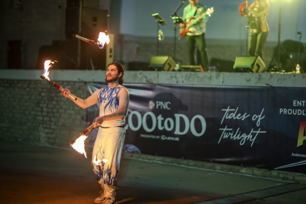 Fire performer twirling torches near outdoor stage